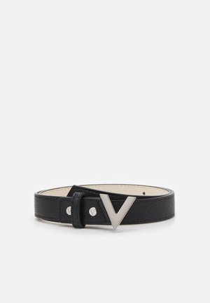 Musta teksturoidusta nahkavyö, jossa on hopeinen V-muotoinen solki ja vastaavat niitit, esillä kierrettynä yksivärisellä taustalla.
