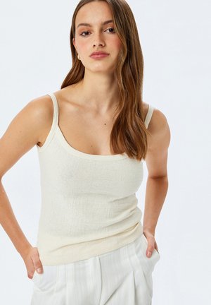 Light beige tank top with a textured fabric, featuring thin straps and a square neckline, paired with striped, tailored pants.