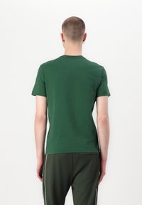 T-shirt verde in cotone con collo rotondo e maniche corte, vista da dietro. Design minimale, texture morbida e silhouette aderente.
