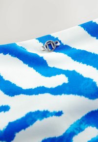 Blaue und weiße Stoff mit einem Tigerstreifenmuster und einem silbernen, kreisförmigen Verschlussdetail in der oberen linken Ecke. Weiche Textur.