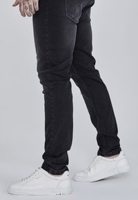 Černé džíny s slim fit, doplněné bílými teniskami se strukturovanou podrážkou a nenápadnými kovovými detaily.