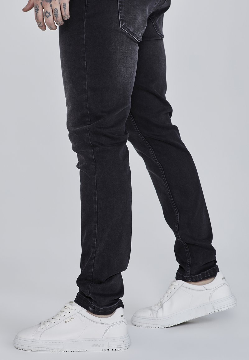 Černé džíny s slim fit, doplněné bílými teniskami se strukturovanou podrážkou a nenápadnými kovovými detaily.