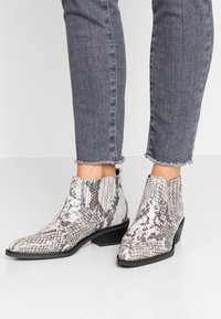 Schwarz-weiße Schlangenleder-Print Stiefeletten mit niedrigem, gestapeltem Absatz, spitzem Schuh und plissierten Details an den Seiten.
