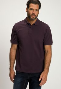 Dunkellila Poloshirt aus Baumwolle mit klassischem Kragen, kurzen Ärmeln und einer Knopfleiste mit drei Knöpfen; getragen mit dunklen Jeans.
