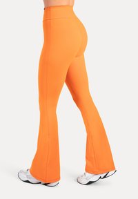 Oranssit liehulahkeiset leggingsit, valmistettu joustavasta ja sileästä kankaasta, jossa on korkea vyötärö ja kontrastitikkaukset. Yhdistä valkoisiin jalkineisiin.