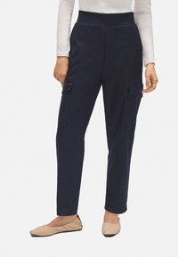 Pantalones cargo azul marino con una cintura alta, que cuentan con dos bolsillos laterales y un ajuste slim, combinados con zapatos planos de color beige claro.