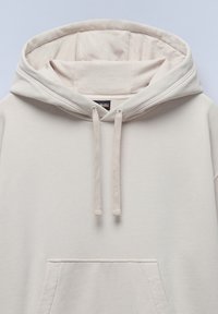Lichtbeige hoodie met een voorzak, een trekkoord bij de hals en zachte, gestructureerde stof. Gladde afwerking en minimalistisch ontwerp.