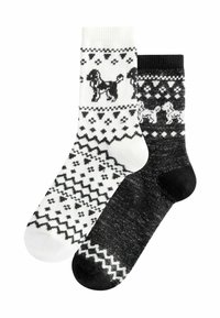 Stricksocken, eine weiß mit schwarzem Hund und geometrischen Mustern, die andere schwarz mit weißen Mustern und kleinen Hundedetails.