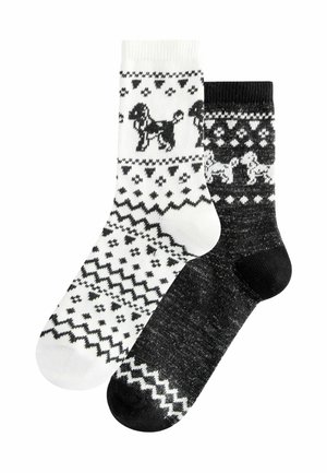 Stricksocken, eine weiß mit schwarzem Hund und geometrischen Mustern, die andere schwarz mit weißen Mustern und kleinen Hundedetails.