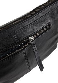 Czarna skórzana torba z metalowym zamkiem błyskawicznym w kolorze srebrnym, częściowo otwarta, ukazująca czarną tkaninę w białe kropki wewnątrz kieszeni.