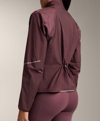 Bordeauxroter Windbreaker mit cinchbarem Saum, reflektierenden Akzenten und hohem Kragen. Leichtes Material mit strukturiertem Finish.