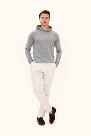 Grå hættetrøje i blødt stof, kombineret med lyse beige bukser og mørkebrune loafers. Model står med armene krydset i en afslappet pose.