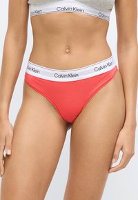 Κοραλλί εσώρουχο σλιπ με λευκή ζώνη μέσης που φέρει το λογότυπο "Calvin Klein" σε μαύρο. Υλικό από απαλό βαμβάκι, σχεδιασμός με ελάχιστη κάλυψη.