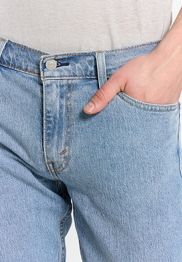 Jeans de mezclilla azul claro con un corte clásico, que presentan costuras en contraste, un bolsillo frontal y un cierre de botón de metal.