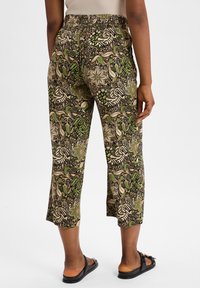 Pantalons courts à motifs en noir, crème et vert avec des designs floraux et de feuillage. Taille élastique et coupe droite. Portés avec des sandales plates.