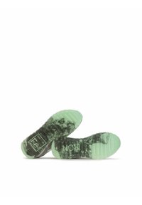 Shoe soles feature a textured design with dark and light green accents. The rubber is flexible and shows a unique pattern with branding.