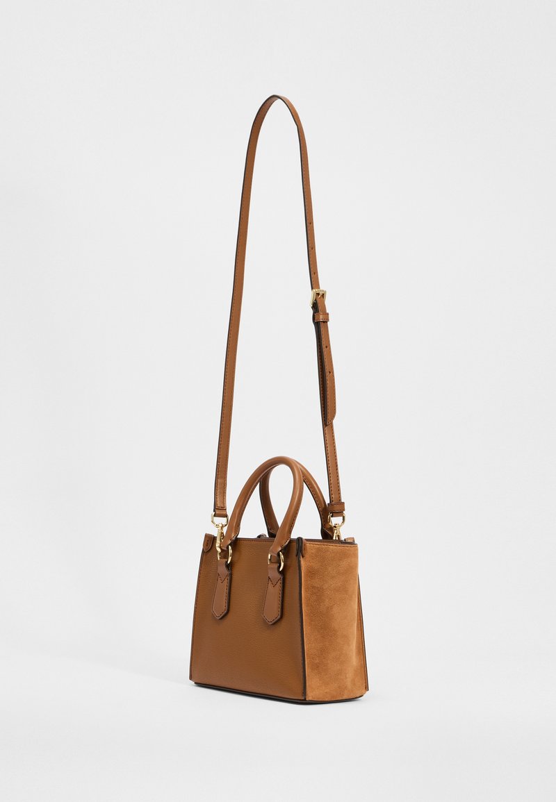 Sac à main marron au design structuré, composé de matériaux en daim et en cuir, avec des poignées doubles et une sangle amovible. Accents en matériel doré.