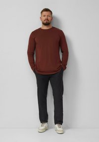 Donkerrode shirt met lange mouwen gecombineerd met donkere broek en witte sneakers. Het shirt heeft een ronde hals, nauwsluitende mouwen en een gladde textuur.