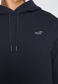 Felpa con cappuccio blu navy in tessuto morbido, con tasca a marsupio e coulisse regolabili. Piccolo logo bianco sul petto.