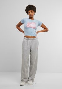 Light blue fitted t-shirt with graphic lips and text "Can I give you a kiss," paired with gray sweatpants and white sneakers.