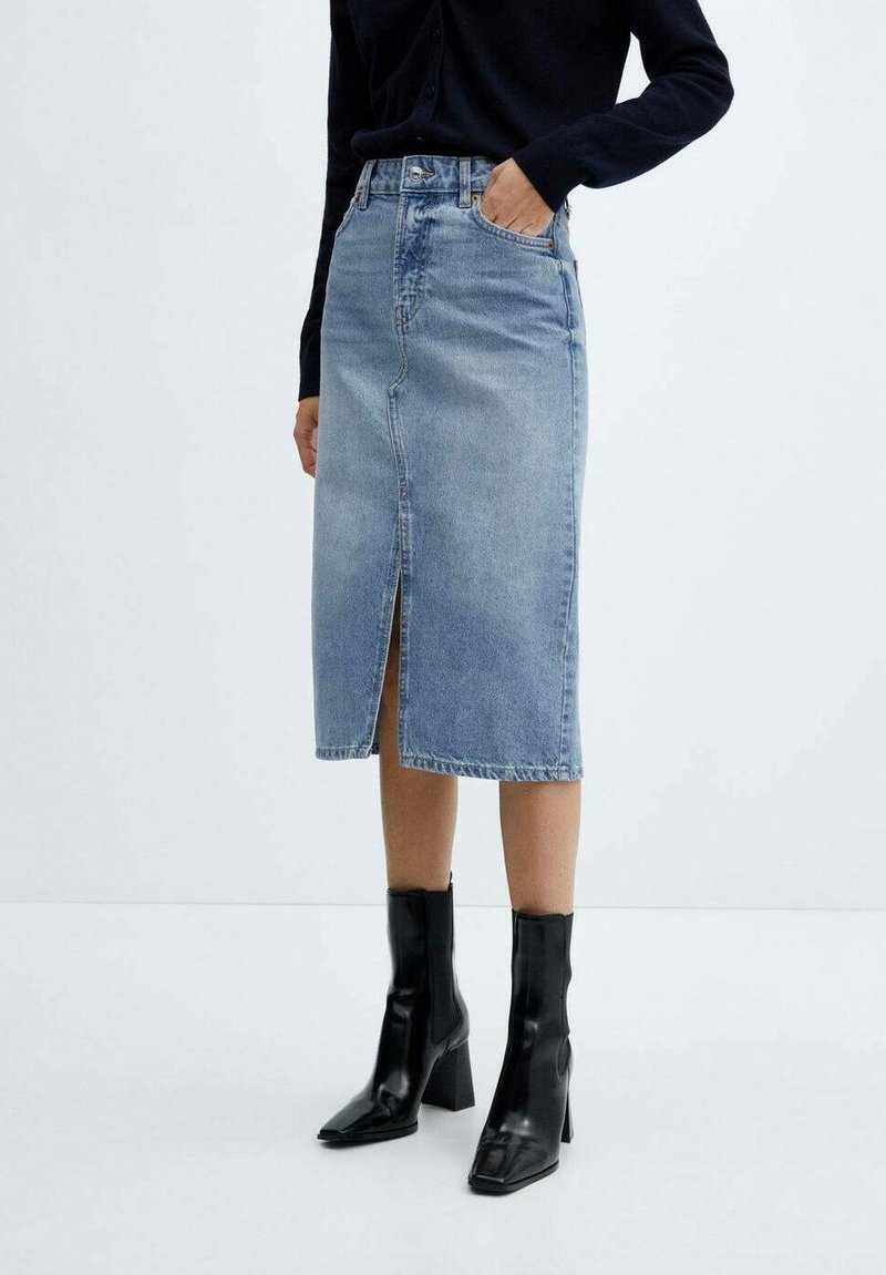 Denim midi krilo v svetlo modri barvi, z razporkom spredaj, visokim pasom in klasičnim krojem, v kombinaciji s črnimi čevlji na peto do gležnjev.