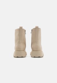 Botines de cuero beige con cremalleras traseras, suelas gruesas y costuras visibles a lo largo de las uniones. Textura suave y diseño minimalista.