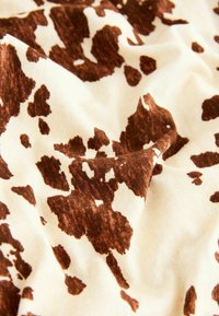 Brown and cream fabric with a cow print pattern, featuring soft texture and a smooth appearance, arranged in gentle folds.