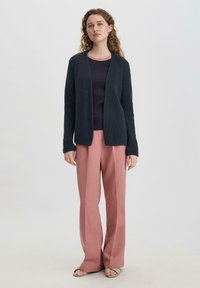 Laivastonsininen neulottu neuletakki tumman paidan päällä, yhdistettynä löysiin vaaleanpunaisiin housuihin. Yksinkertainen muotoilu, pehmeä rakenne ja avoin etuosa.