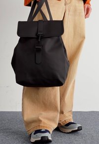 Zaino nero con patta pieghevole, spallacci regolabili e una fibbia centrale. Realizzato in materiale morbido, presenta un design minimalista.
