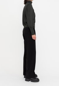 Dunkelgrüner, taillierter Rollkragenpullover mit puffartigen Ärmeln, kombiniert mit hochgeschnittenen schwarzen Hosen und klobigen schwarzen Plateaustiefeln.