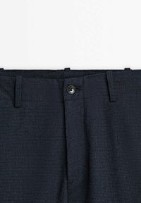Pantalon en tissu texturé bleu foncé avec un bouton noir et des passants de ceinture à la taille sur fond blanc.