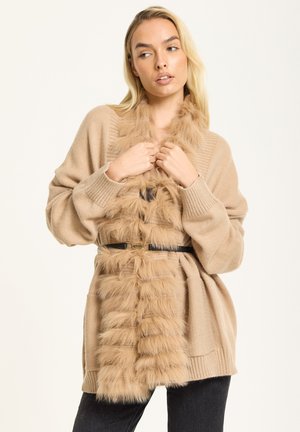 Beige cardigan with a fur-like texture along the front. Features a long, open design and a black belt with a gold buckle.