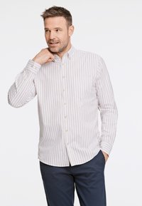 Camisa de botones a rayas finas en beige y blanco, de tela de algodón, con un bolsillo en el pecho y cuello clásico, combinada con pantalones navy.