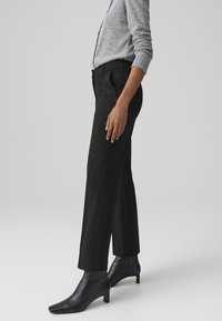 Pantaloni neri su misura con un design a gamba dritta, caratterizzati da un tessuto liscio e dettagli di cucitura sottili. Abbinati a stivaletti neri con punta.