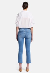 Jeans azzurri chiari a vita alta con orlo cropped e sfilacciato. Fit sagomato e due tasche posteriori. Indossati con una camicia bianca con bottoni.