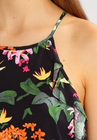 Top halter floreale con sfondo nero, caratterizzato da foglie e fiori vivaci nei colori rosa, giallo e verde, realizzato in tessuto leggero.