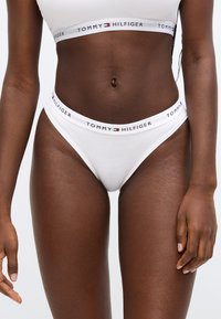 Biele bavlnené tangá s elastickým pásom s logom "TOMMY HILFIGER" v čiernej a červenej farbe. Jemná textúra, priliehavý strih.