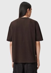 Brązowy bawełniany t-shirt z krótkimi rękawami i prostym krojem. Posiada minimalne logo na karku z tyłu. Gładka tekstura.