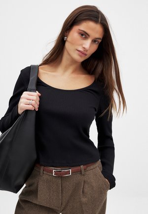 Mustat ribattuja pitkähihainen paita, jossa on pyöreä pääntie, yhdistettynä ruskeisiin houndstooth-housuihin ja mustaan nahkaiseen olkalaukkuun.