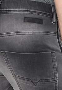 Grå denimjeans med en baksidesficka designad med en framträdande läderetikett "Diesel". Diskret urtvättning och kontrasterande sömnadsdetaljer är synliga.