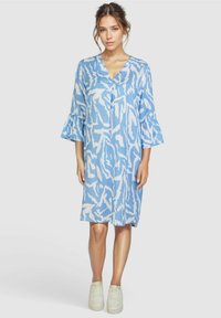 Blau-weiß gemusterte Kleid mit V-Ausschnitt, Glockenärmeln und knielanger Länge. Kombiniert mit weißen Sneakers für einen lässigen Look.
