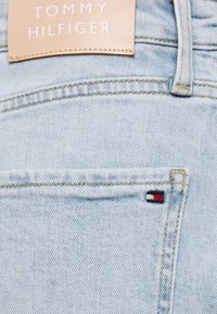 Vaaleansiniset farkut, joissa on nahkainen Tommy Hilfiger -logo. Takapuolella on pieni brodeerattu logo punaisena, valkoisena ja mustana.