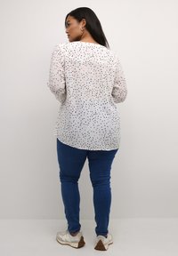 Bílá košile s dlouhými rukávy a černými a růžovými puntíky, kombinovaná se modrými skinny džíny a bílými teniskami s hnědými podrážkami.