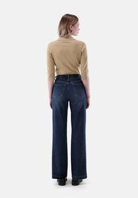 Hellbraunes geripptes Stricktop mit Dreiviertelärmeln, kombiniert mit dunkelblauen hoch taillierten weiten Jeans und schwarzen Schuhen. Einfaches Design.