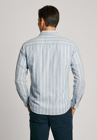 Gaiši zils svītrains krekls, izgatavots no mīksta auduma, ar garām piedurknēm un pogu aprocēm, iekļaujot izliekto apakšmalu un vertikālām baltām svītrām.