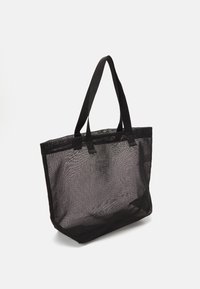 Sac cabas noir en maille avec deux poignées solides, de forme rectangulaire, ouverture supérieure, et surface texturée. Design minimaliste sans accents supplémentaires.