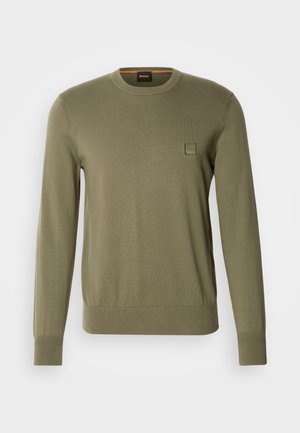 Olive green sweater with long sleeves, crew neck, ribbed cuffs and hem, featuring a subtle logo patch on the chest in a square format.