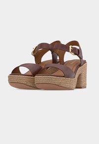 Sandales compensées en cuir marron avec larges brides, boucles dorées et talons blocs épais en jute tissée sur fond blanc.