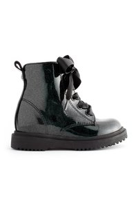 Stivaletto nero lucido con glitter, suola spessa, allacciatura con lacci a nastro larghi e tab in tessuto sul retro.