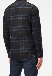 Camisa de cuadros negra con líneas azules, con puños abotonados y yugo trasero, fabricada en una tela suave con un acabado ligeramente texturizado.